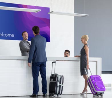 Two people with suitcases checking in at a front desk