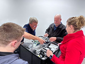 4 people looking at the interior of a projector, learning how to maintain it.