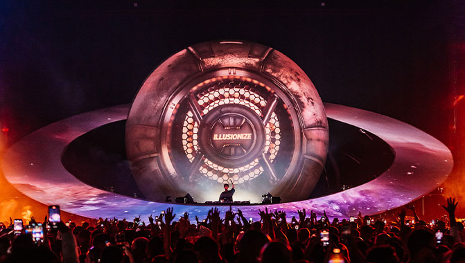 A crowd in front of a large replica of Saturn and its ring that is projection mapped with the word "Illusionize".