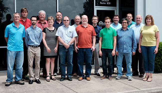 Group of people posed in front of the glass fa&ccedil;ade of a commercial building.