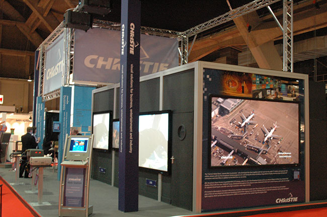 A tradeshow booth with the word &ldquo;Christie&rdquo; shown throughout and three large screens on the booth walls.
