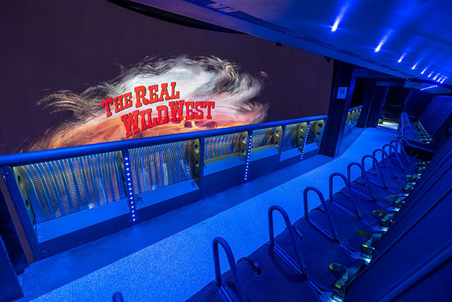 Empty seats in front of a large screen that reads &ldquo;The real wild west&rdquo;.