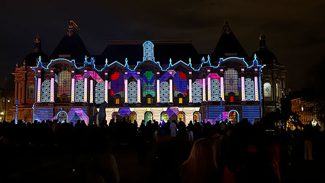 The façade of a building is projection mapped with various colors and patterns.