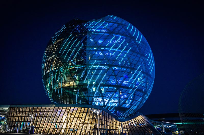 A large spherical building is lit in blue at night.