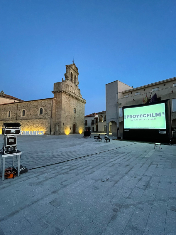 A large movie screen is set up in a central square at dusk.