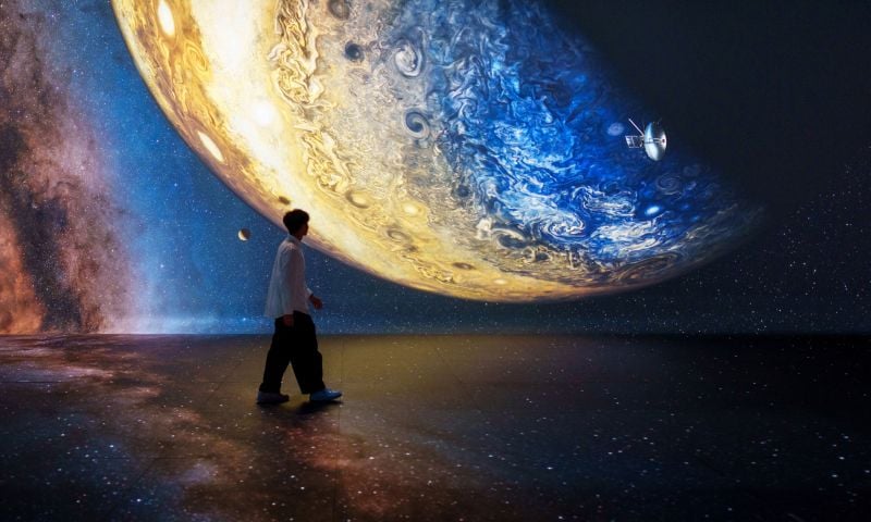 A person standing in front of a wall with a projected image of the earth.