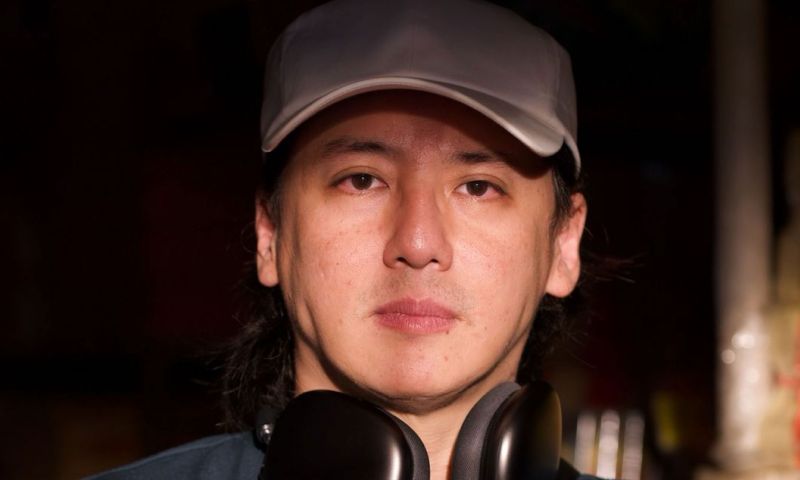 Close up of a man wearing a baseball hat and headphones around his neck.