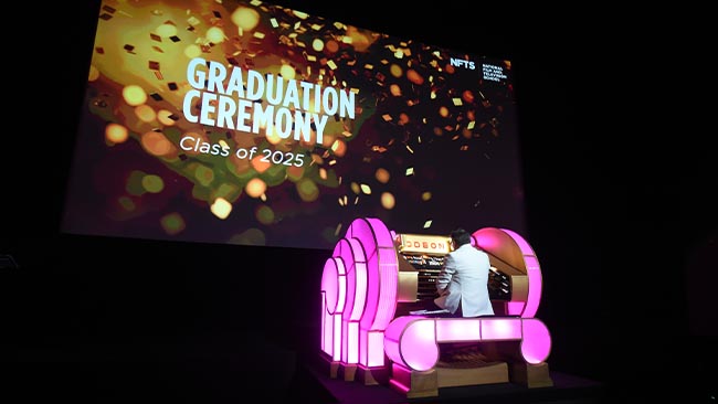 A person sits at an illuminated organ on a large stage.