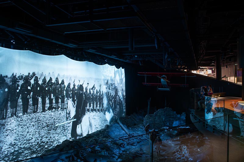 A balcony overlooks a diorama of a battle scene with a large screen displaying projected images.