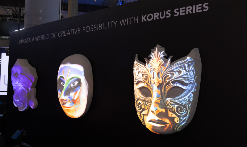White masks mounted on a dark background are projection mapped with vivid colors.