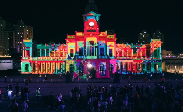 The façade of a large building is projection mapped with vibrant colors.
